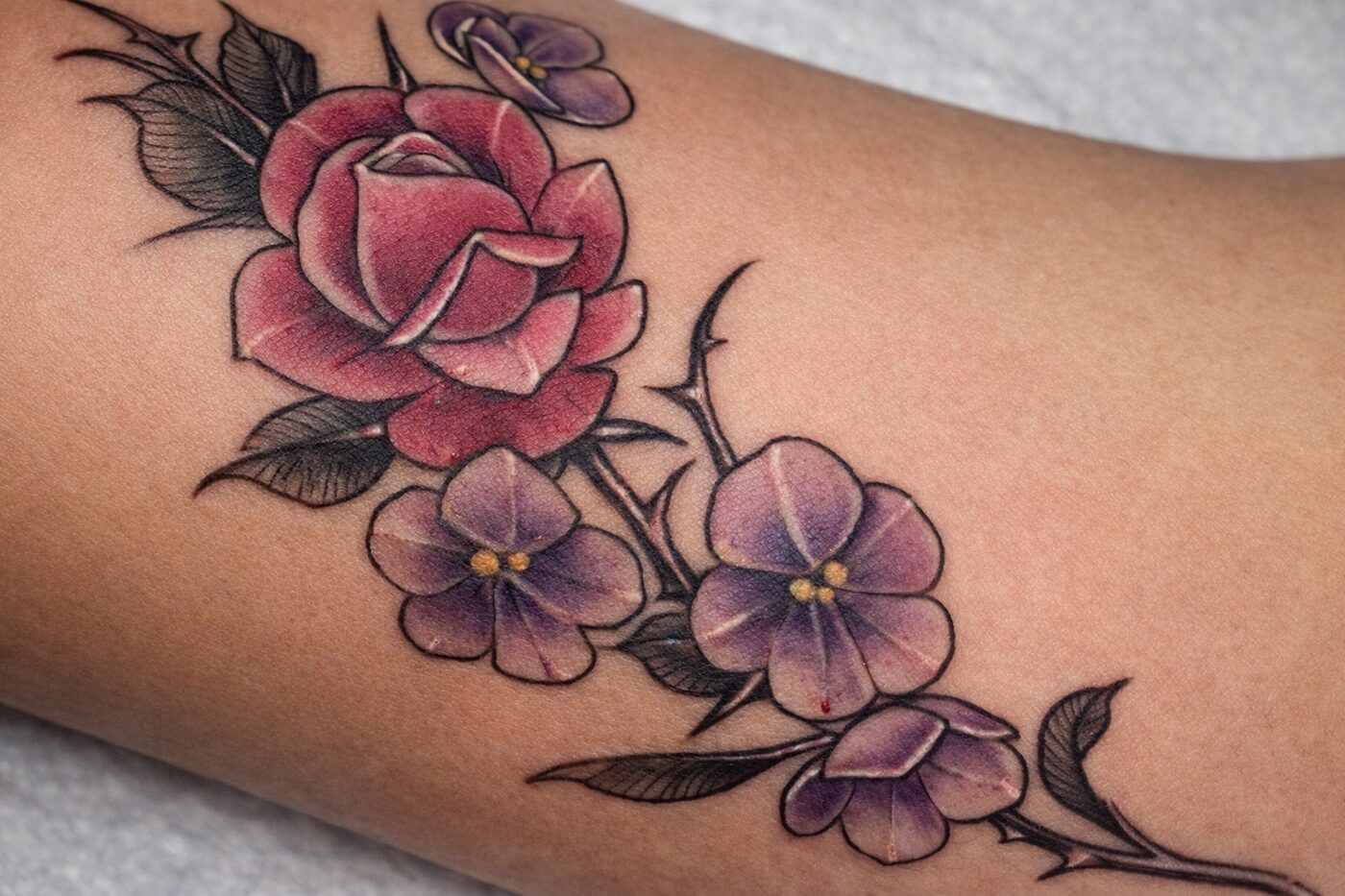 Delicate birth-flower tattoo of a rose and violets by Jeremy Swan