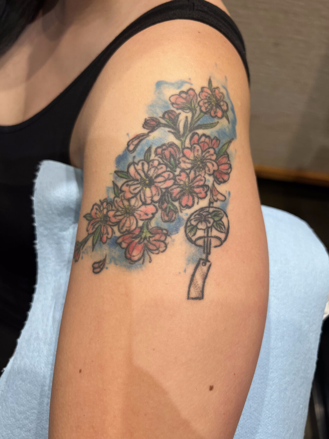 Faded watercolor cherry-blossom tattoo on the shoulder before a cover-up