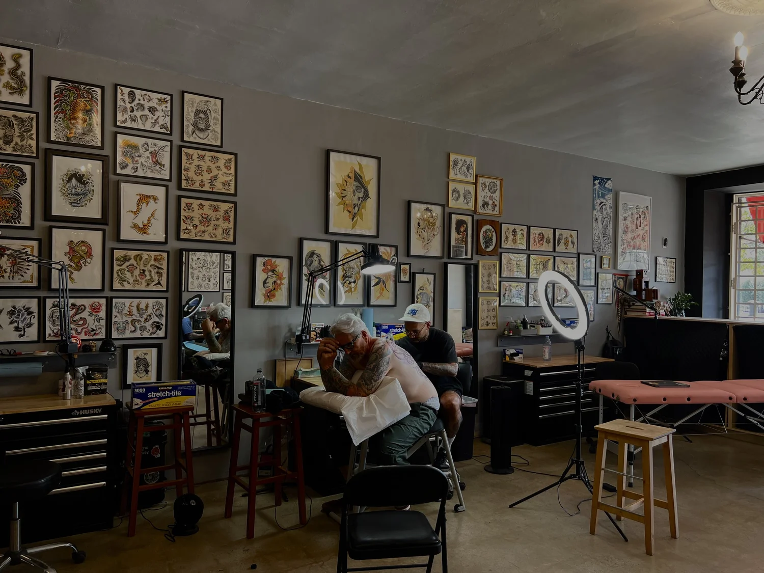 Artist tattooing a client beside framed flash